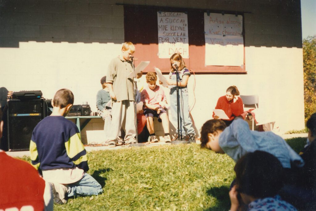 Shule Sukkes celebration at Naivelt, children stage a Sukkes play (“Fun Camp tsu shule… fun shule tsu Camp”)