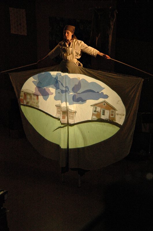 A performer on stilts carries a painted banner during the Oy di Velt pageant